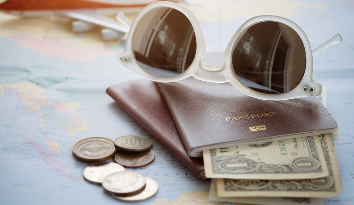 Sunglasses sitting on top of a passport that's holding dollar bills.
